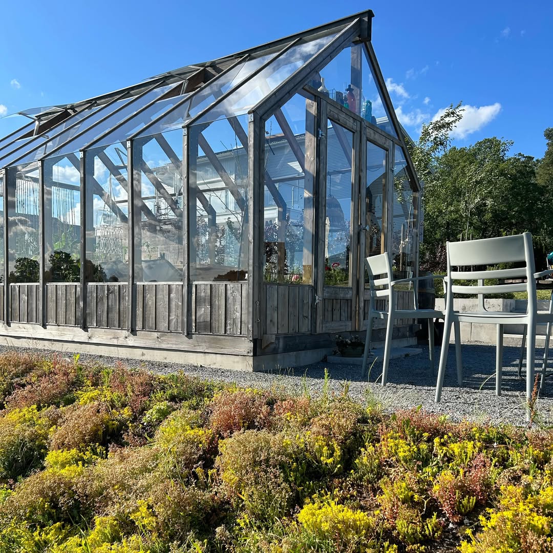Glass greenhouse with wooden frame and chairs in a garden setting
