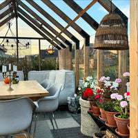 Indoor garden with potted plants, table, chairs, and a woven lampshade.