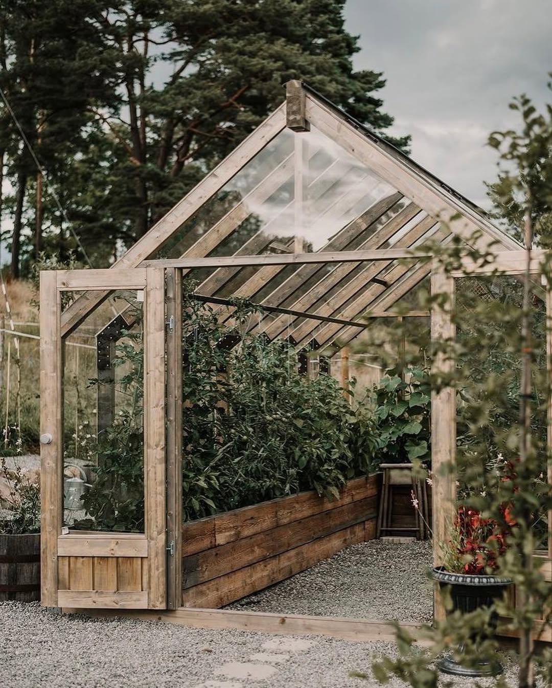 Wooden greenhouse with glass panels surrounded by trees and plants