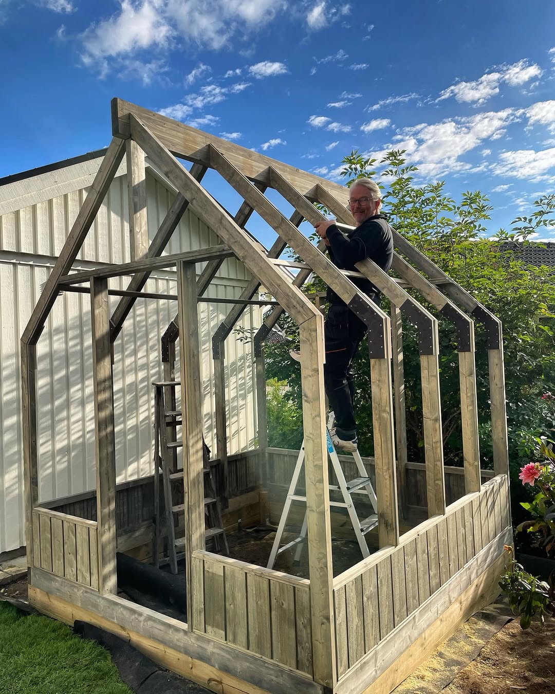Person building a wooden playhouse in a garden with a clear blue sky.